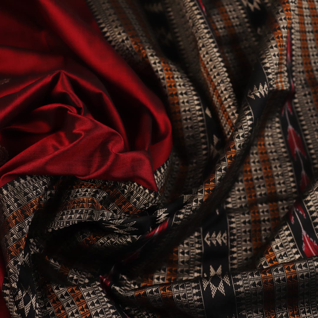 Close-up texture of handwoven Bomkai silk saree fabric: maroon and black threads forming butta pattern.