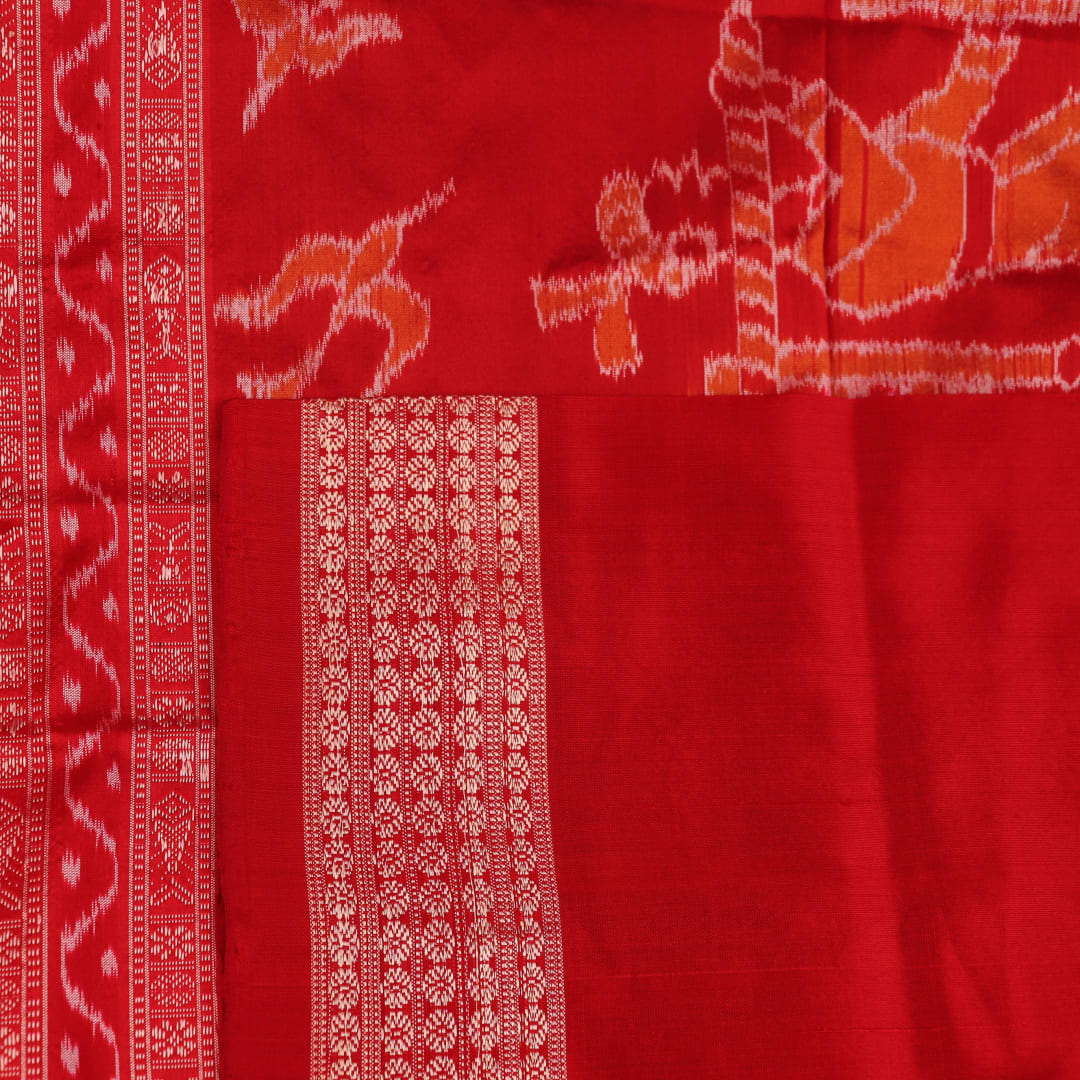 Close-up of a peach and red Sambalpuri silk saree fabric showing the intricate handloom texture and motifs.
