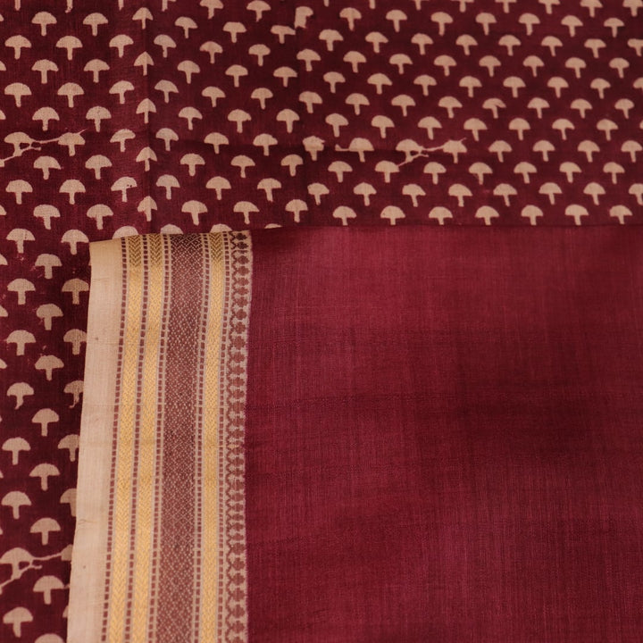 Close-up of maroon Tussar silk saree fabric, showing natural slub texture and printed pattern.