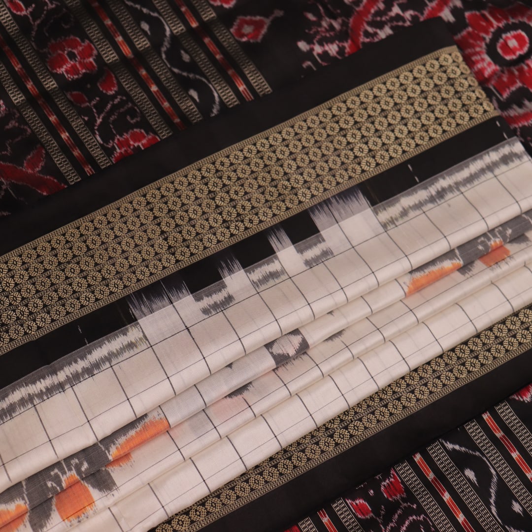 Close-up of handloom Sambalpuri silk saree fabric texture; white with subtle black motifs.