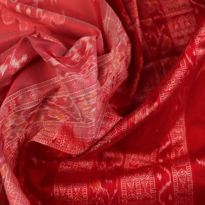 Close-up of a peach and red Sambalpuri silk saree fabric showing the intricate handloom texture and motifs.