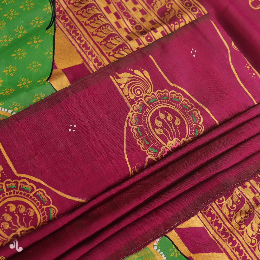 Close-up of magenta Patachitra silk saree fabric texture showing handloom weave and paint details.