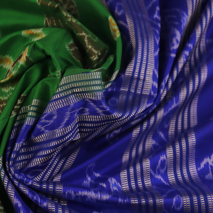 Close-up of green and blue Sambalpuri silk saree fabric showing intricate handloom weave and motif details.