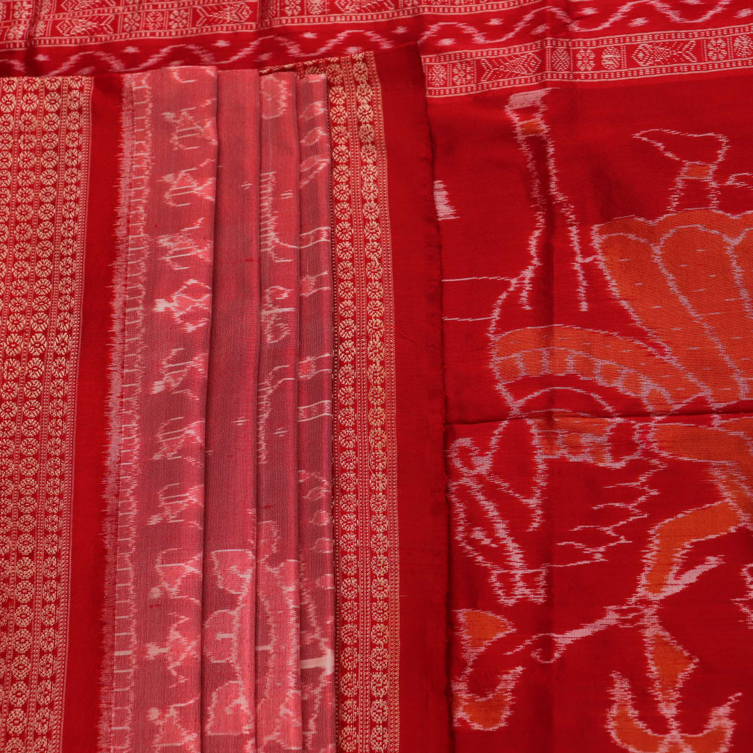 Close-up of a peach and red Sambalpuri silk saree fabric showing the intricate handloom texture and motifs.