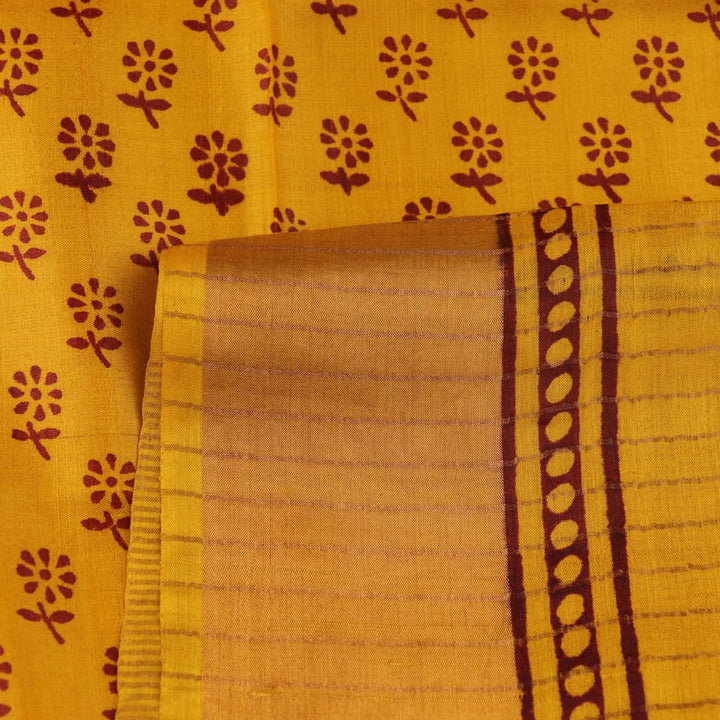 Close-up of the yellow printed Tussar silk saree's distinct slubby fabric texture.