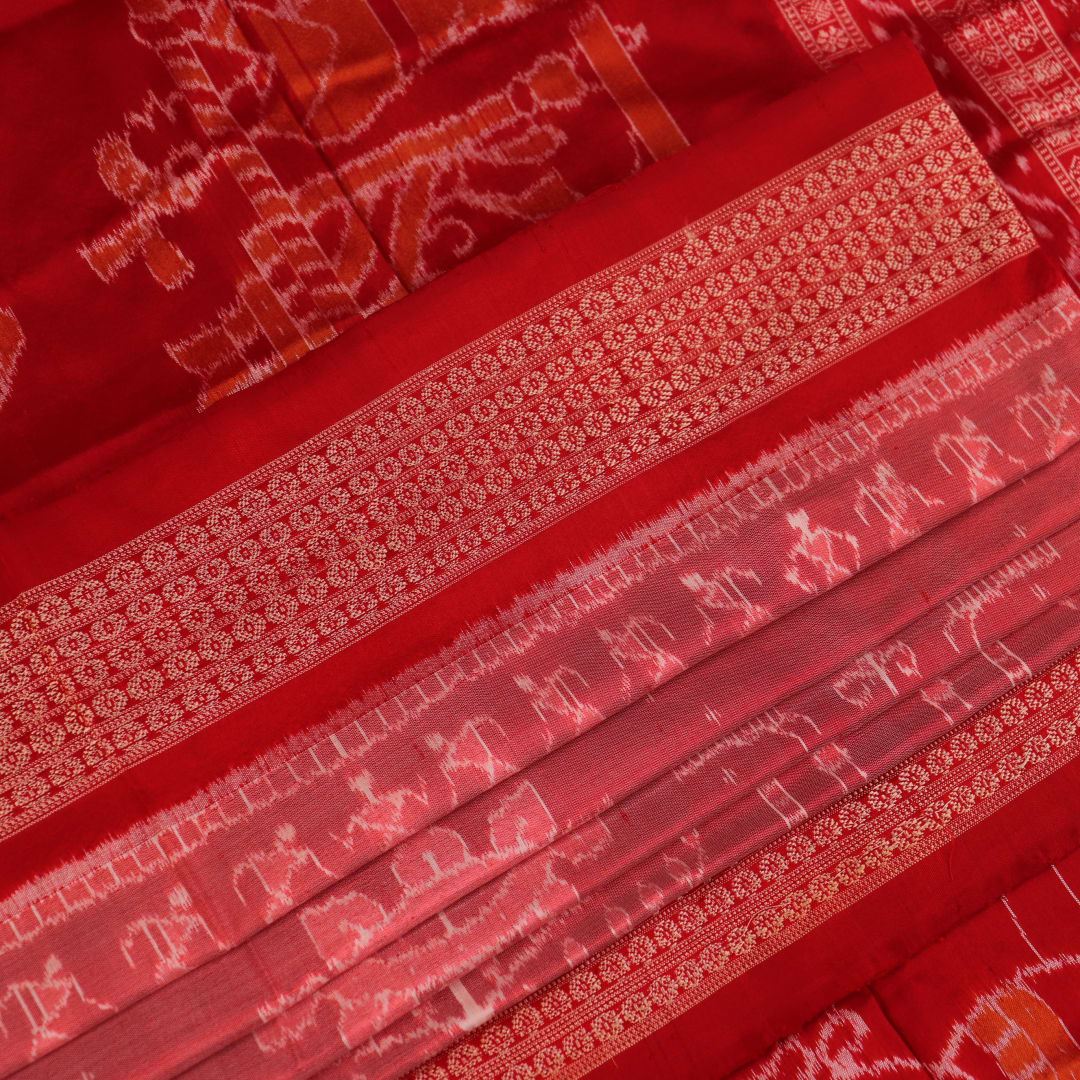 Close-up of a peach and red Sambalpuri silk saree fabric showing the intricate handloom texture and motifs.