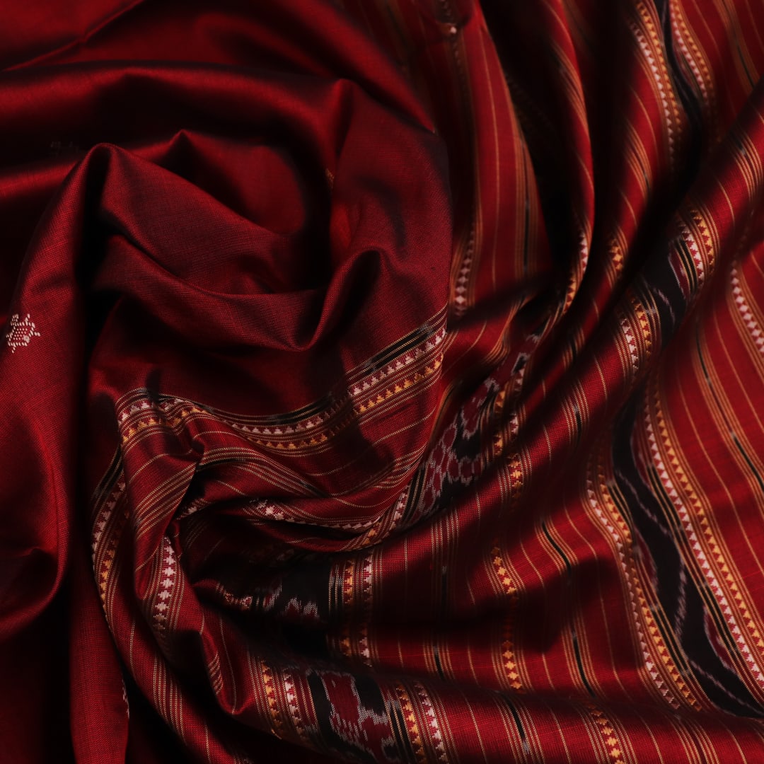 Close-up of maroon Sambalpuri Silk Saree fabric, showing intricate butta weave texture.