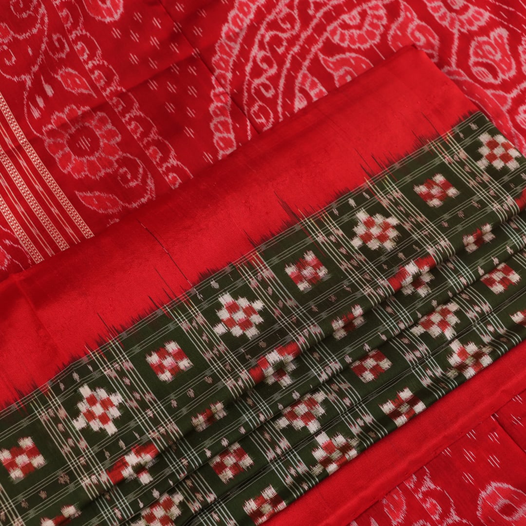 Close-up of green Sambalpuri silk saree fabric showing intricate woven motif texture and red thread details.