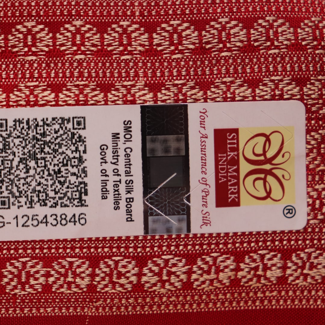 Close-up of a peach and red Sambalpuri silk saree fabric showing the intricate handloom texture and motifs.