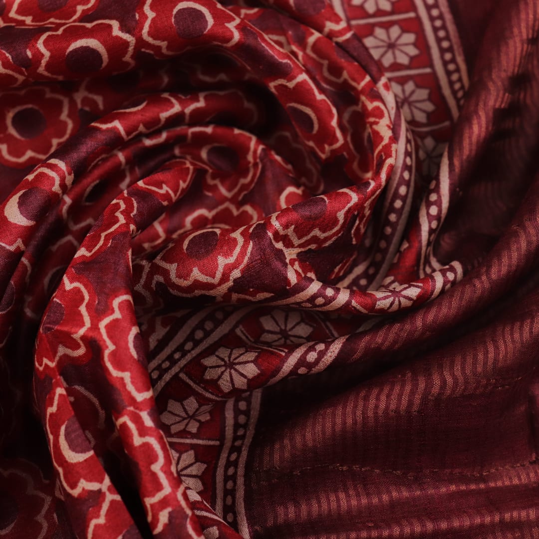 Close-up of maroon Tussar silk saree fabric, revealing its characteristic slub texture and printed details.