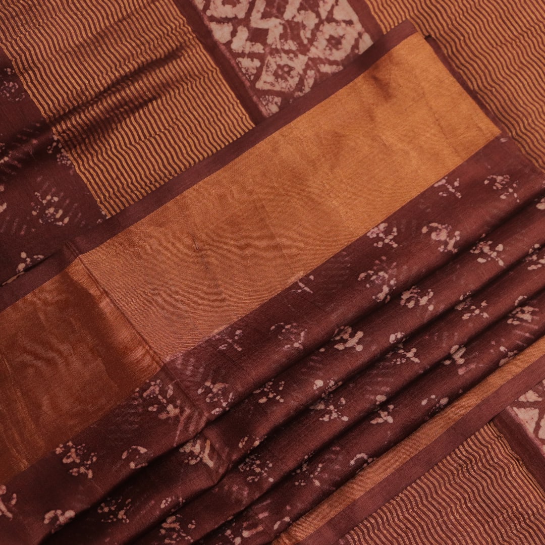 Close-up of the brown Tussar silk saree fabric, highlighting its natural slub texture and printed pattern.