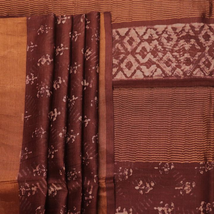 Close-up of the brown Tussar silk saree fabric, highlighting its natural slub texture and printed pattern.