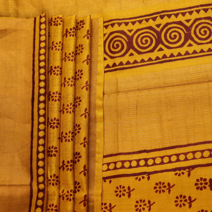Close-up of the yellow printed Tussar silk saree's distinct slubby fabric texture.