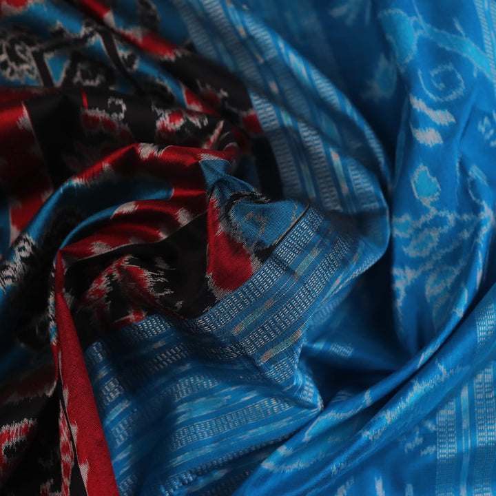 Close-up of multi-color Sambalpuri silk saree fabric showing texture and woven motifs; secondary color blue visible.