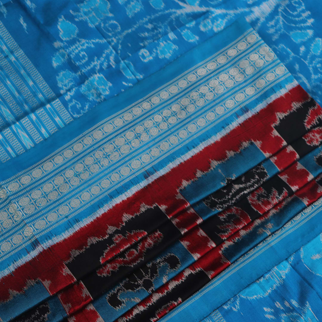 Close-up of multi-color Sambalpuri silk saree fabric showing texture and woven motifs; secondary color blue visible.