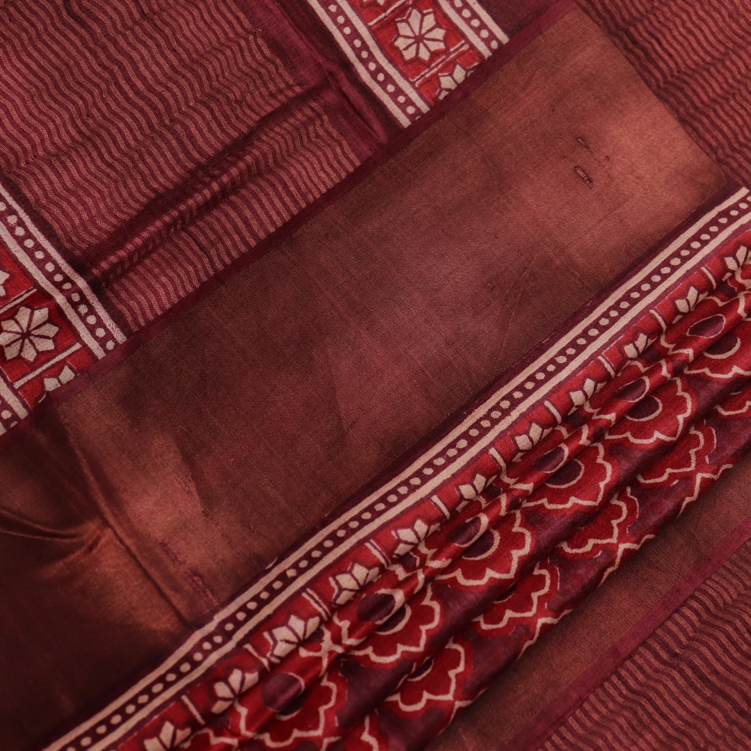Close-up of maroon Tussar silk saree fabric, revealing its characteristic slub texture and printed details.