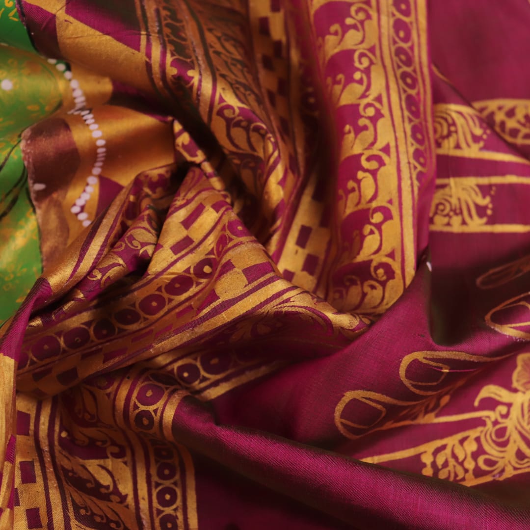 Close-up of magenta Patachitra silk saree fabric texture showing handloom weave and paint details.