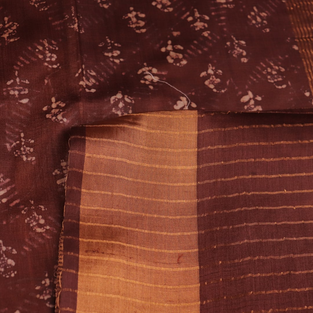 Close-up of the brown Tussar silk saree fabric, highlighting its natural slub texture and printed pattern.