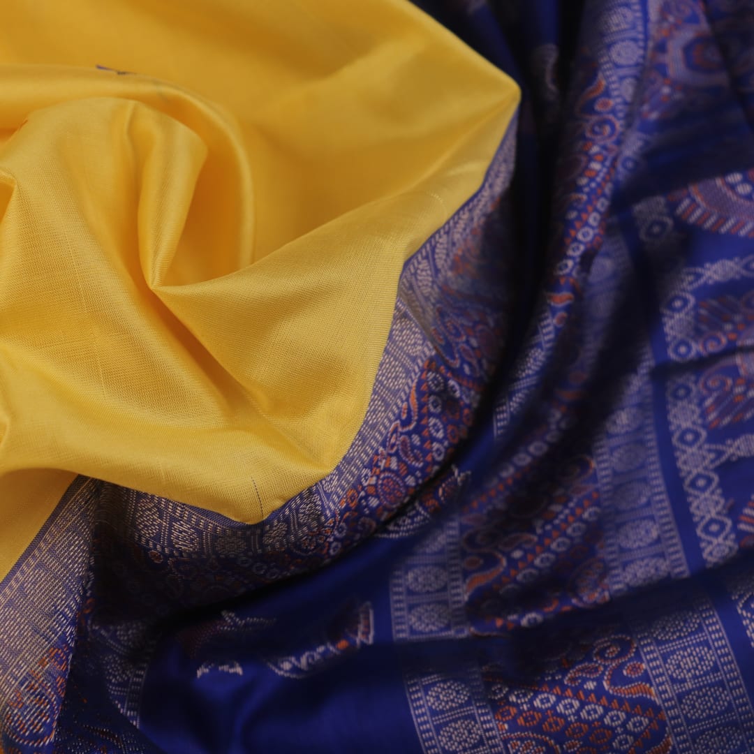 Textured close-up of yellow Bomkai silk saree fabric with blue butta pattern.
