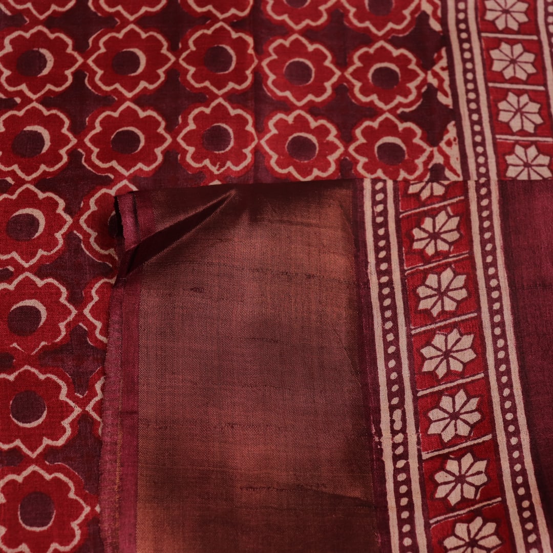 Close-up of maroon Tussar silk saree fabric, revealing its characteristic slub texture and printed details.