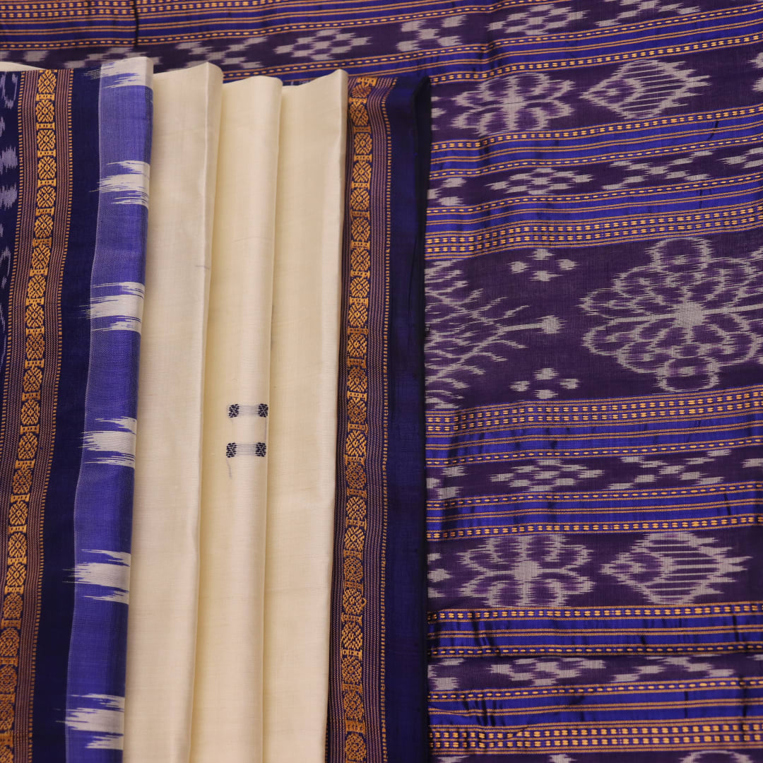 Woman elegantly draped in a white and blue Khandua silk saree with butta pattern.