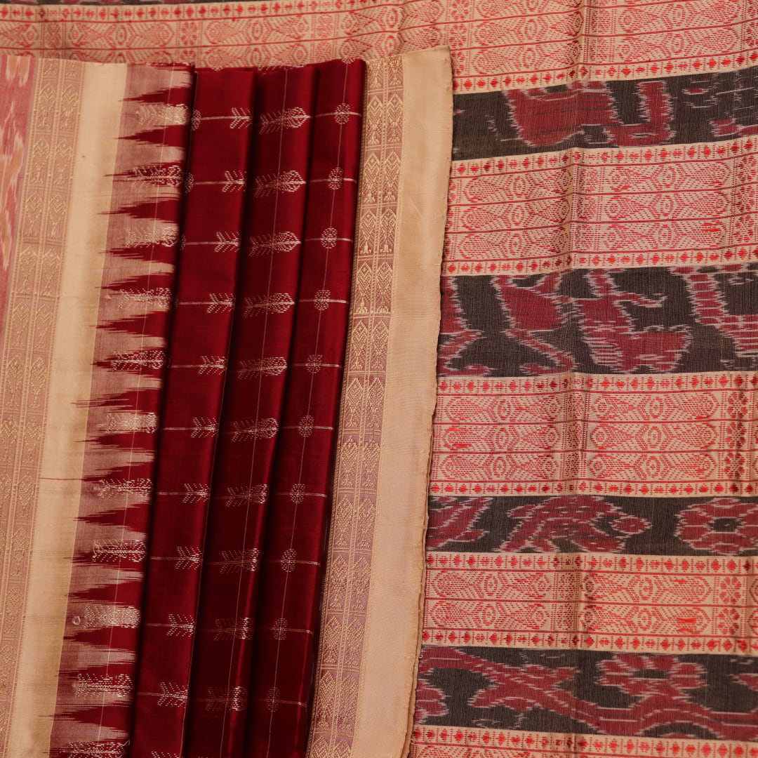 Close-up view of the richly textured silk fabric of a maroon and off-white Sambalpuri saree, featuring a delicate butta pattern.