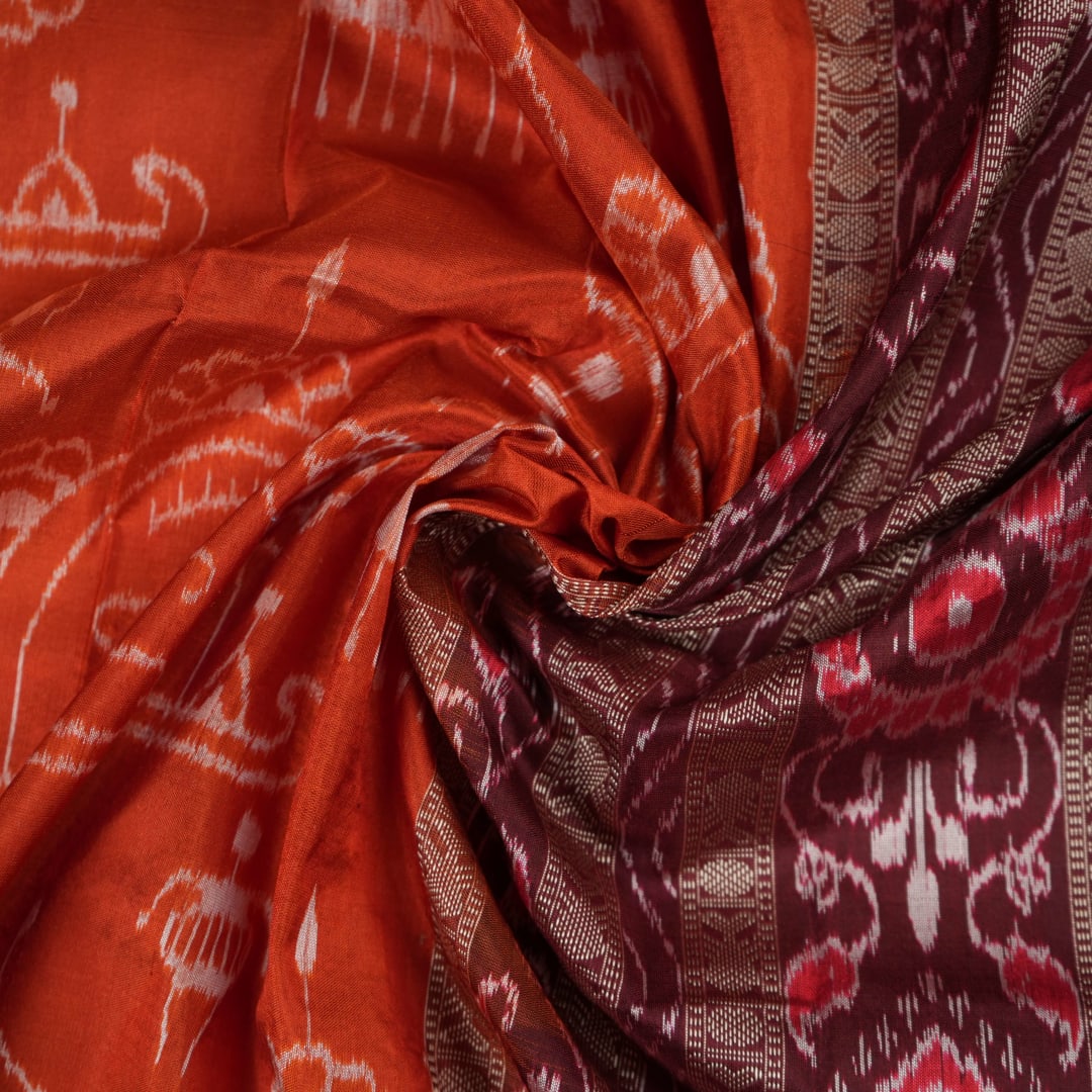 Extreme close-up of the lustrous rust Sambalpuri silk fabric, showing its fine weave and subtle motif texture.