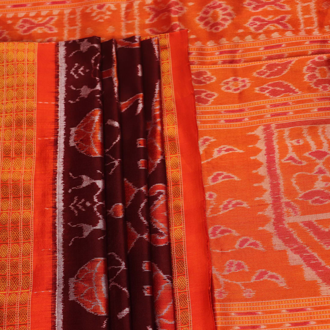 Close-up of maroon and orange Sambalpuri silk saree fabric texture, showcasing handloom weave and motif details.