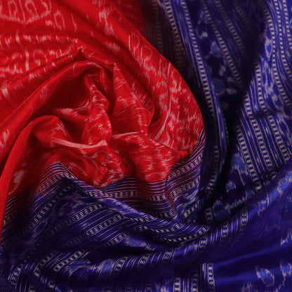 Close-up of red Sambalpuri silk saree fabric showing intricate woven motif texture and subtle blue threads.