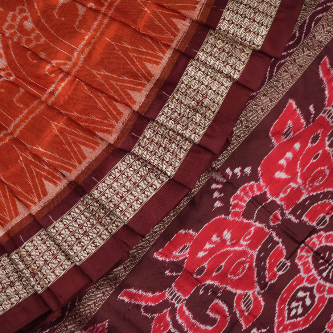 Extreme close-up of the lustrous rust Sambalpuri silk fabric, showing its fine weave and subtle motif texture.