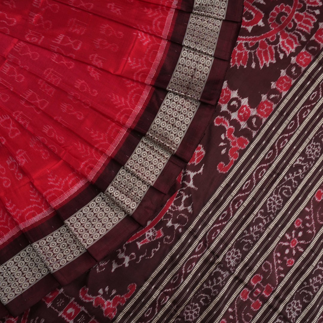 Ultra close-up of the red Sambalpuri silk saree fabric, revealing its luxurious texture and handloom weave.