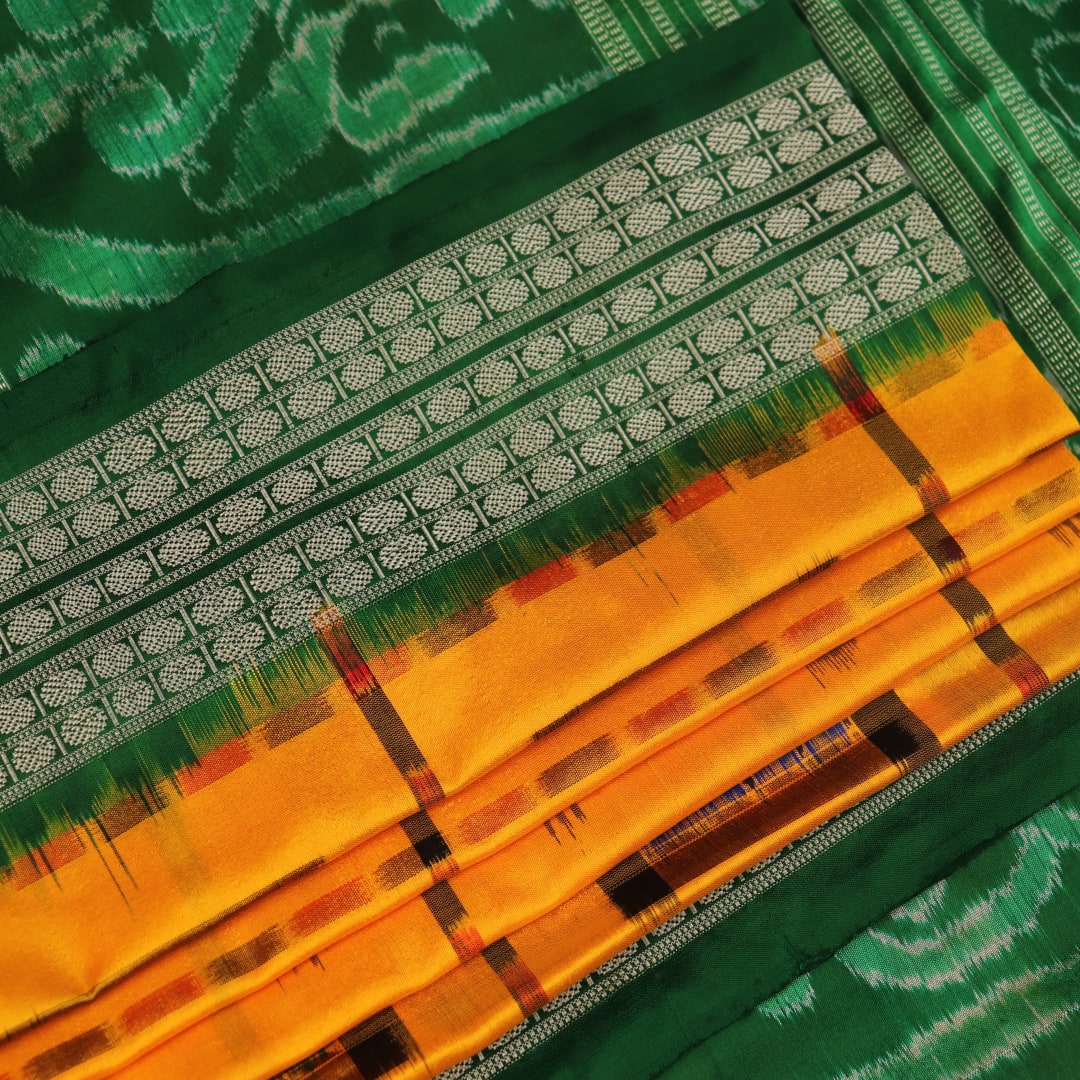 Close-up of yellow Sambalpuri silk saree fabric showing intricate motifs and woven texture.