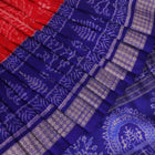 Close-up of red Sambalpuri silk saree fabric showing intricate woven motif texture and subtle blue threads.