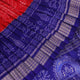 Close-up of red Sambalpuri silk saree fabric showing intricate woven motif texture and subtle blue threads.