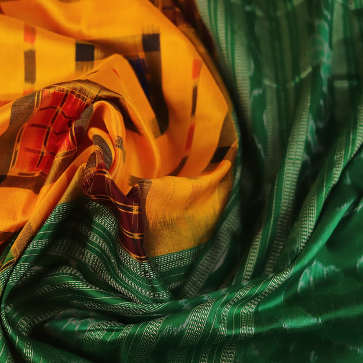Close-up of yellow Sambalpuri silk saree fabric showing intricate motifs and woven texture.
