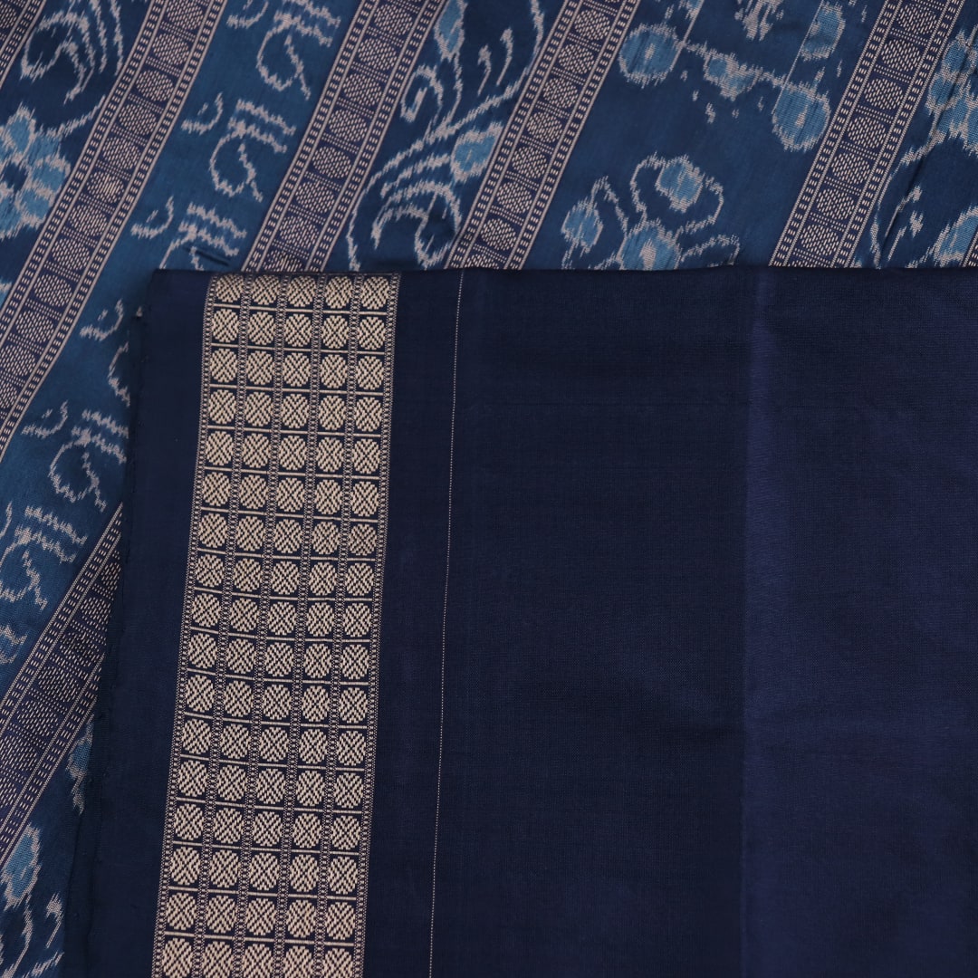 Close-up detail of the cream-colored silk fabric texture with blue motifs in Sambalpuri saree