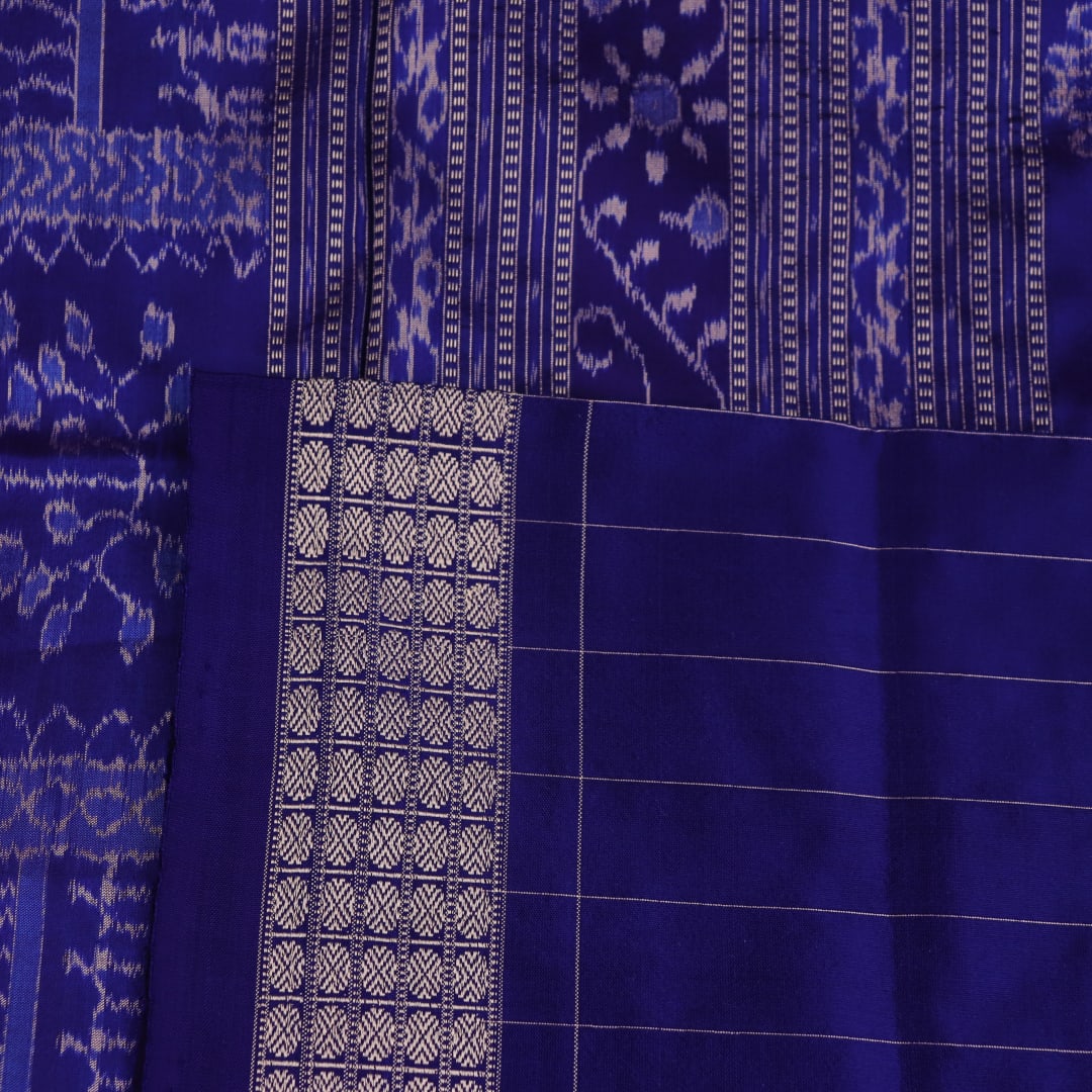 Close-up of red Sambalpuri silk saree fabric showing intricate woven motif texture and subtle blue threads.