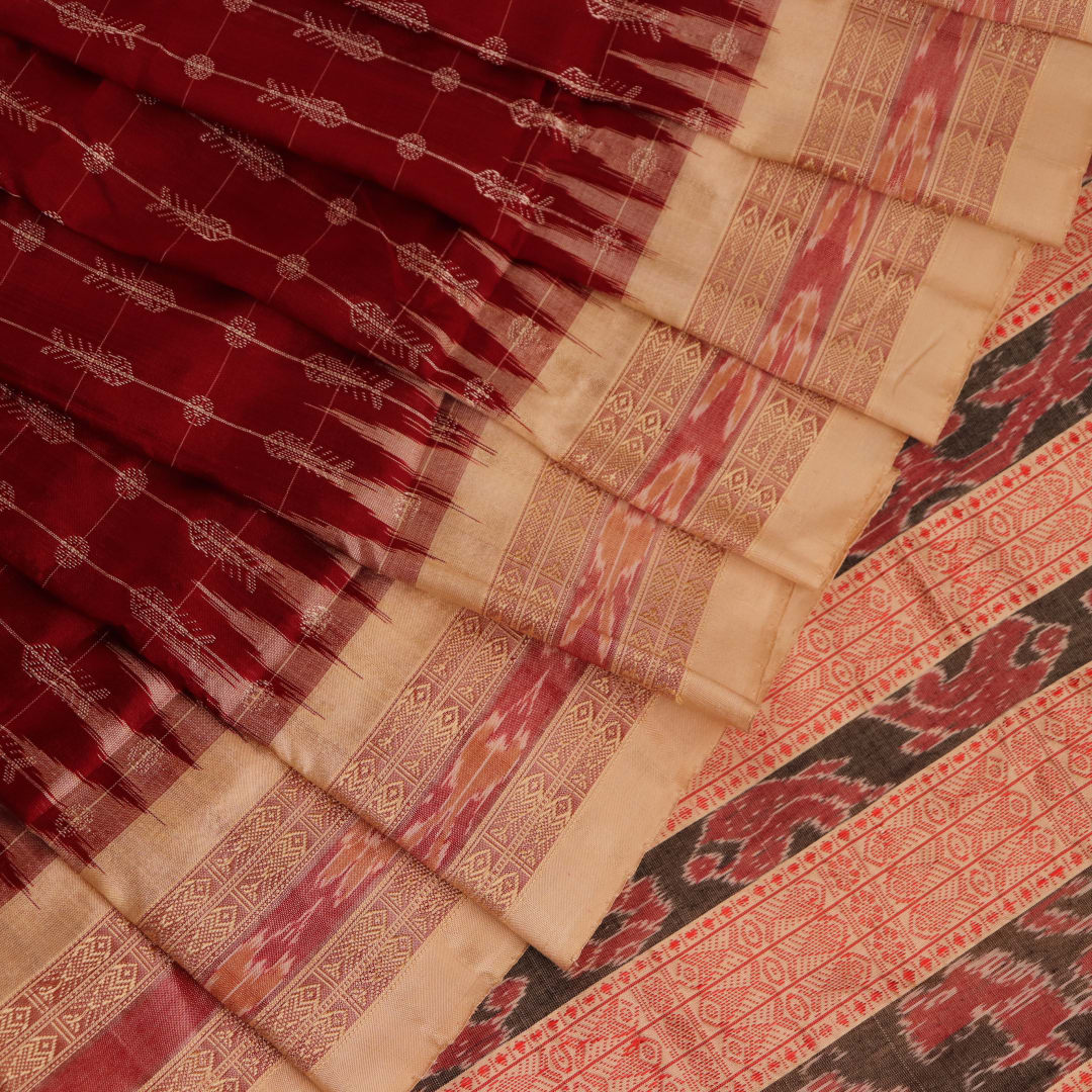 Close-up view of the richly textured silk fabric of a maroon and off-white Sambalpuri saree, featuring a delicate butta pattern.