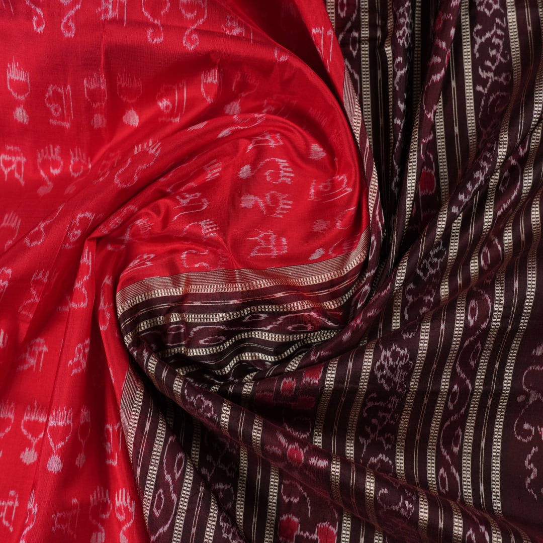 Ultra close-up of the red Sambalpuri silk saree fabric, revealing its luxurious texture and handloom weave.