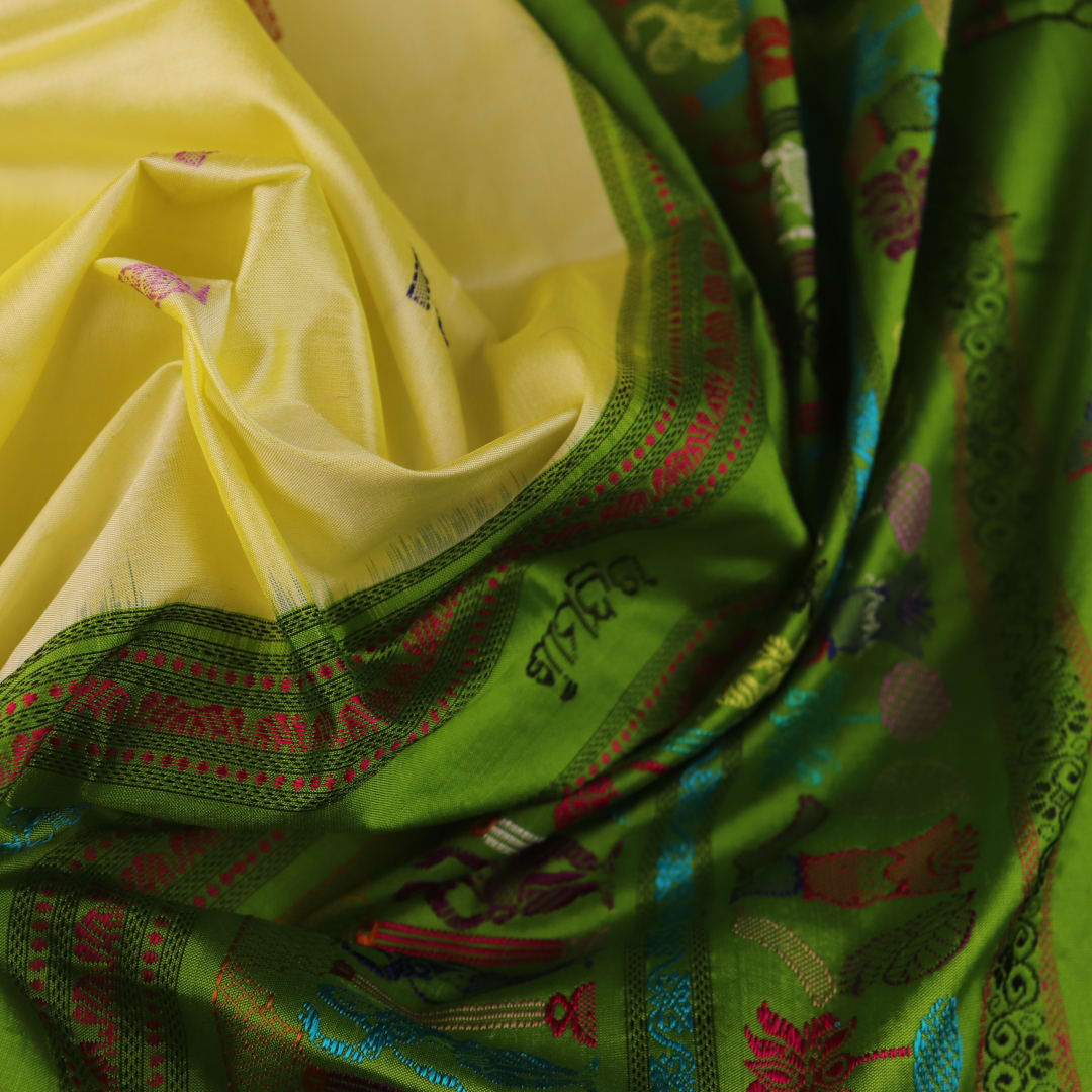 Close-up of cream and green Bomkai Silk Saree fabric texture with butta pattern.