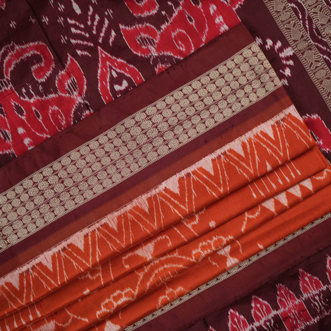 Extreme close-up of the lustrous rust Sambalpuri silk fabric, showing its fine weave and subtle motif texture.