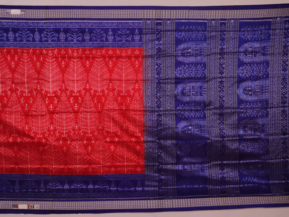 Close-up of red Sambalpuri silk saree fabric showing intricate woven motif texture and subtle blue threads.