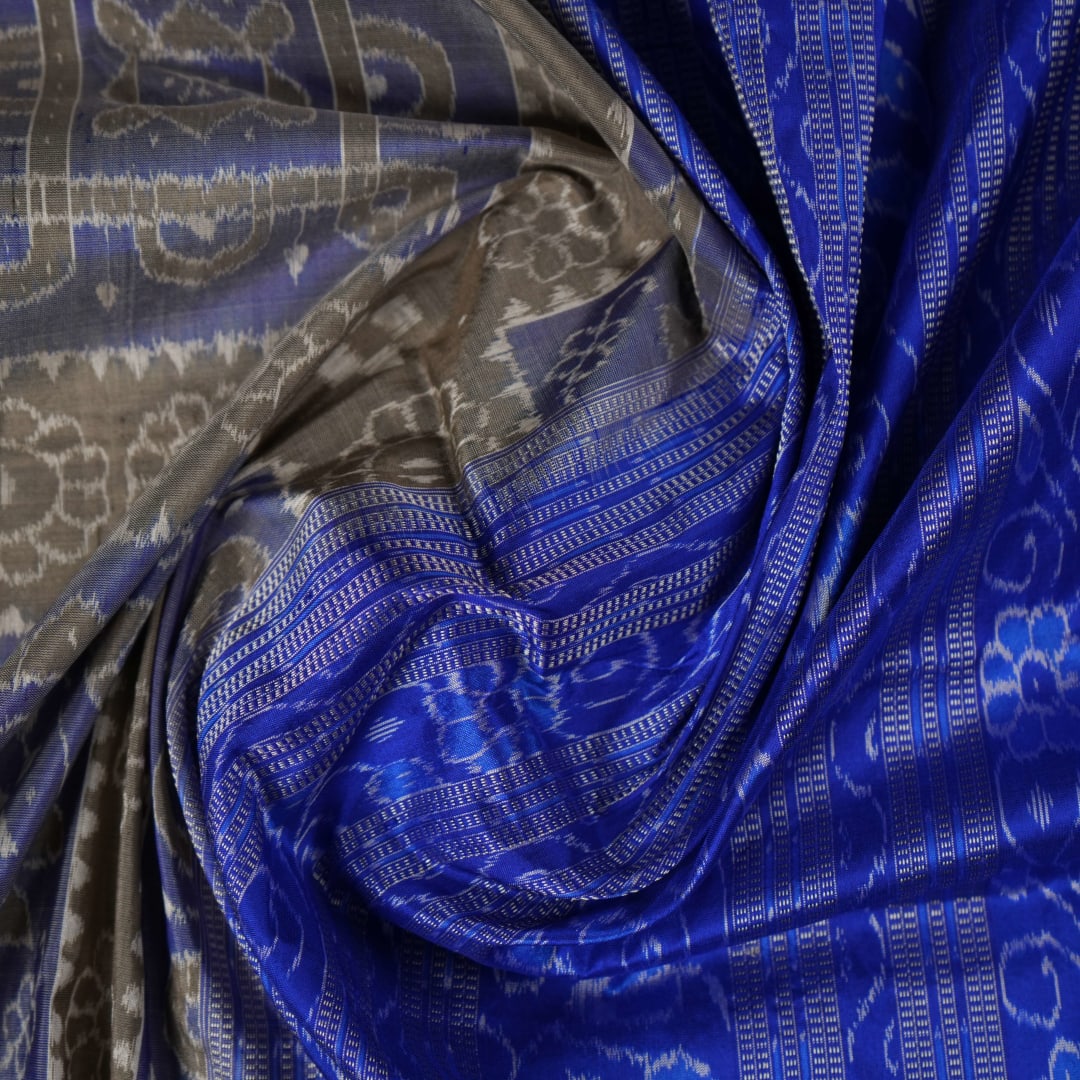Extreme close-up of the grey and blue Sambalpuri silk saree fabric, revealing its rich texture and intricate weave.