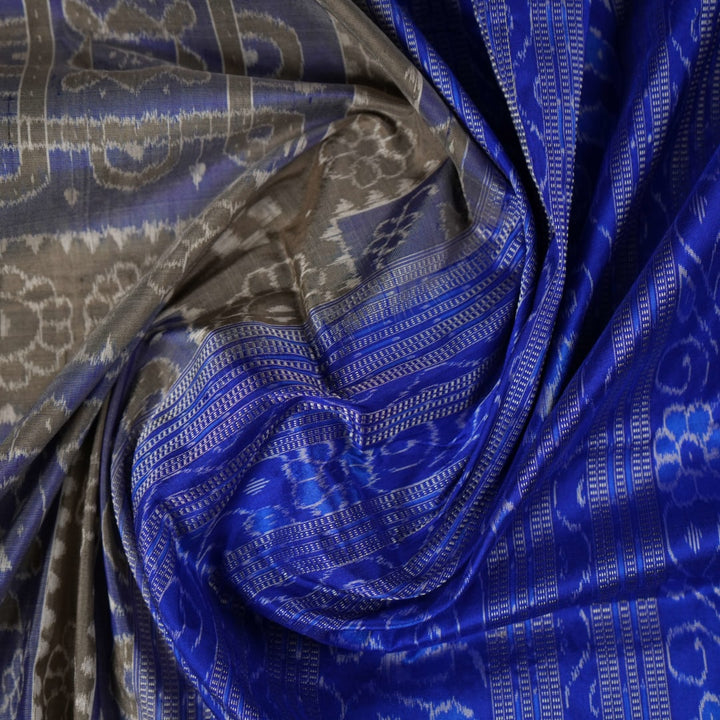 Extreme close-up of the grey and blue Sambalpuri silk saree fabric, revealing its rich texture and intricate weave.