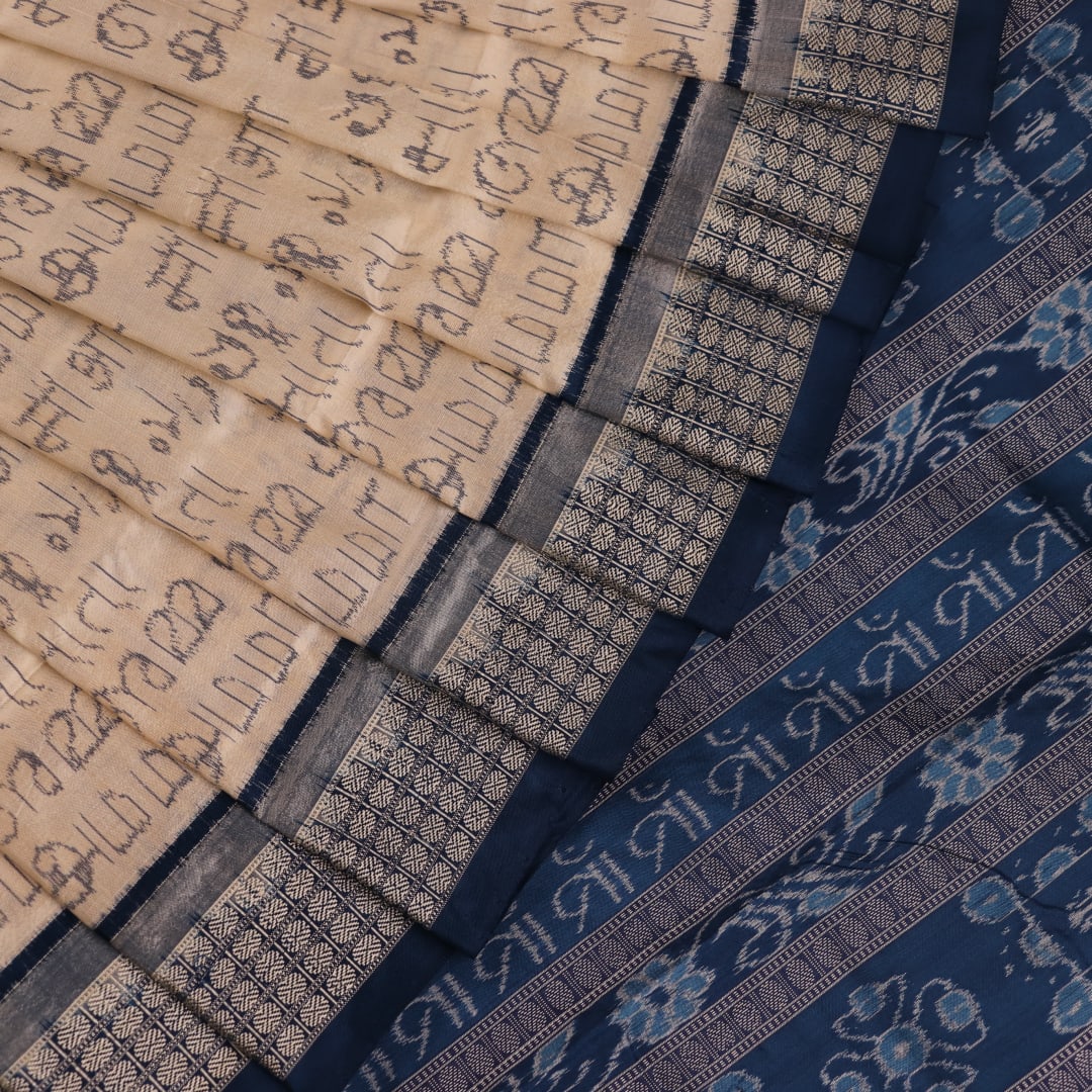 Close-up detail of the cream-colored silk fabric texture with blue motifs in Sambalpuri saree