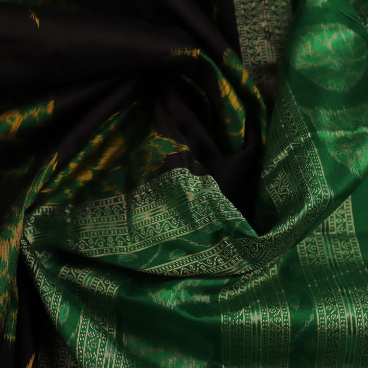 Close-up of the finely textured silk fabric in black, adorned with intricate Sambalpuri motifs in green