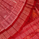 Close-up of a peach and red Sambalpuri silk saree fabric showing the intricate handloom texture and motifs.