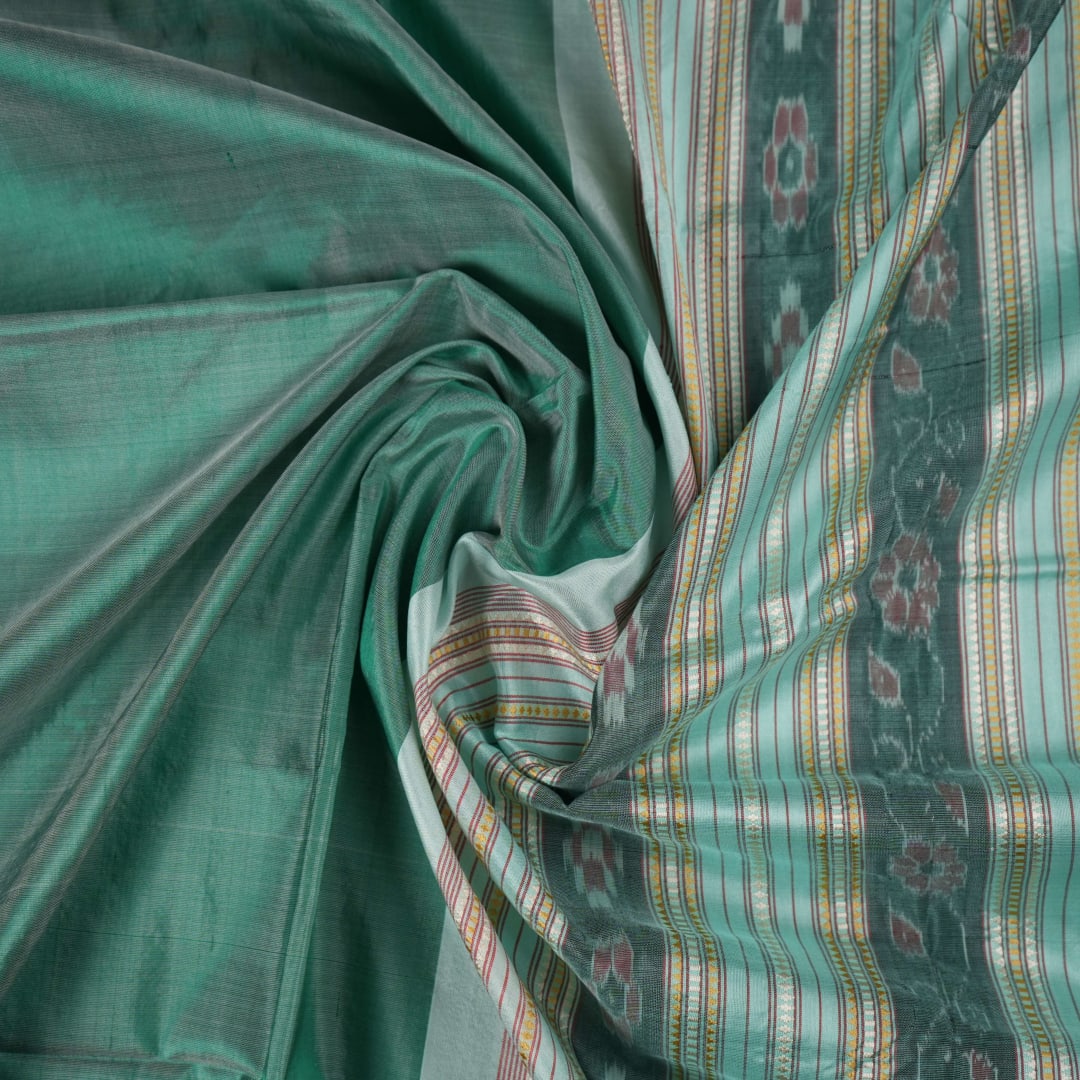 Extreme close-up of the green Sambalpuri silk fabric, revealing its luxurious texture and fine handloom weave.