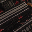 Close-up of the textured silk fabric of a black Sambalpuri saree showing intricate motifs.