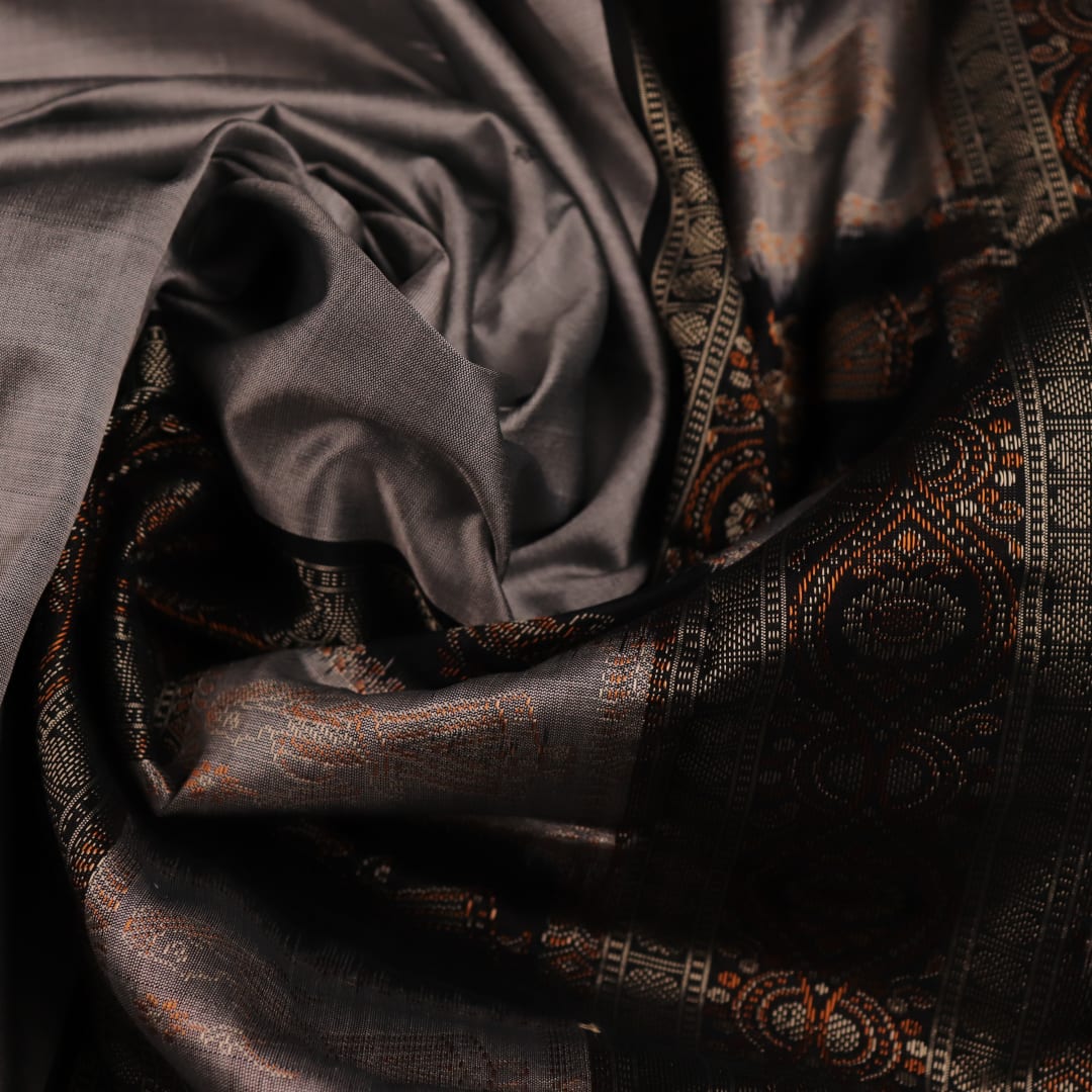 Close-up of intricate silk fabric texture in grey and black, featuring a traditional Bomkai butta pattern